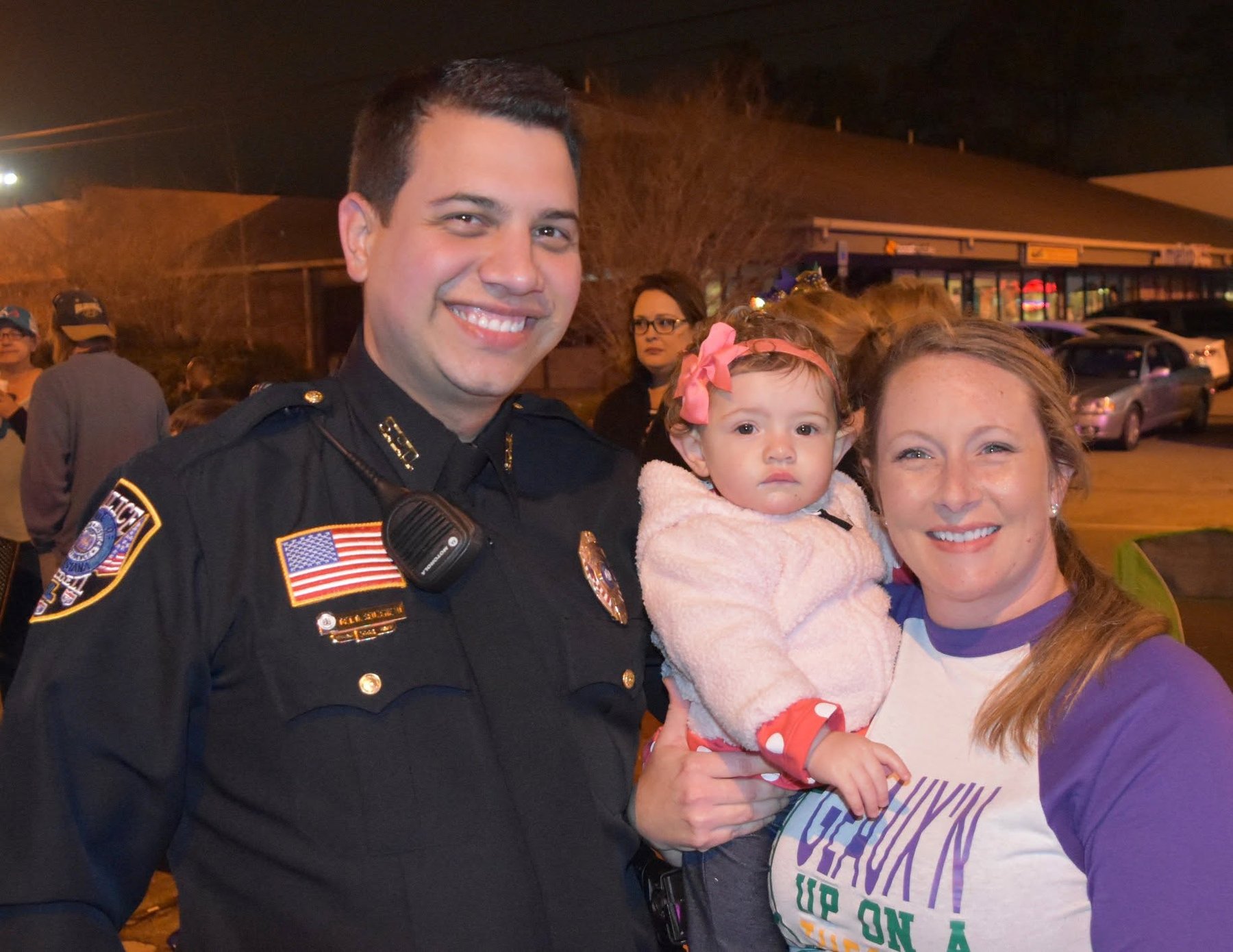 Daniel Seuzeneau in uniform smiling with a mother and her daughter at a Slidell night parade
